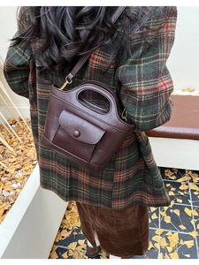 Detail of dark brown leather crossbody bag styled with a plaid autumn coat on fallen leaves