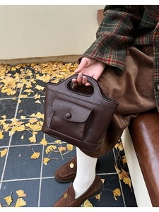 Detail of a dark brown crossbody bag with unique cutout handle and front flap pocket