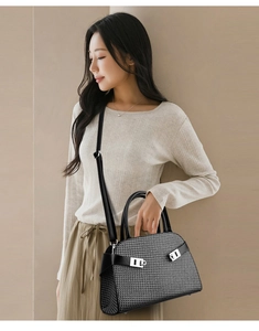 Detail of black woven texture and silver metal turn-lock closures on a trapezoid handbag