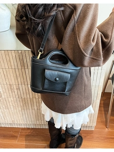 Detail of black trapezoid leather bag with cutout handle and shoulder strap worn by a model