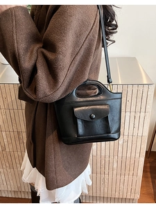 Detail view of black textured faux leather bucket bag with oval handle and button pocket