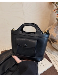 Close-up of black matte handheld bag featuring gold metal rings and front snap pocket