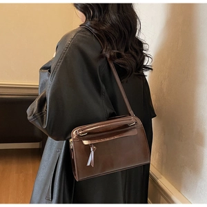 Dettaglio borsa a tracolla in pelle marrone scuro con frange e anello in metallo dorato