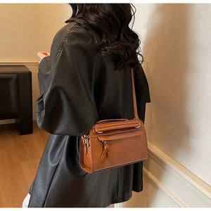 Dettaglio di una borsa a tracolla vintage in pelle marrone con giacca di pelle nera