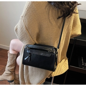 Dettaglio borsa a tracolla nera lucida con nappa, indossata sopra un maglione beige