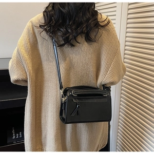 Dettaglio borsa a tracolla in pelle nera con nappine annodate su maglione beige