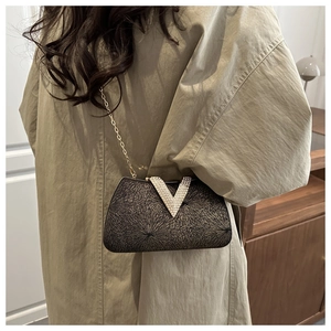Close-up of black evening clutch with sparkling gold patterns and V-shaped diamond buckle
