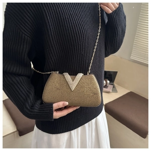 Detail of golden hard-shell clutch bag with rhinestone V-buckle and elegant metal chain