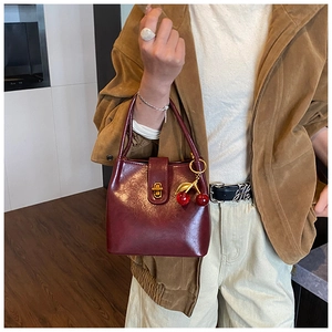 Détail du sac seau bordeaux avec fermoir doré tournant et breloque cerise élégante