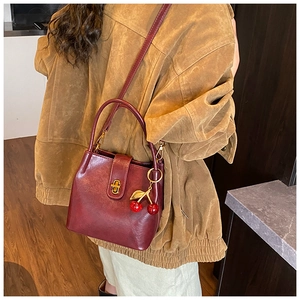 Sac seau en cuir bordeaux avec fermoir doré tournant et pendentif cerise rouge