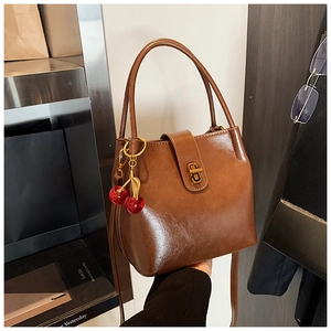 Détail d'un sac seau marron avec fermoir doré et charme cerise rouge décoratif