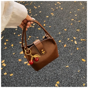 Détail du sac seau en cuir marron avec pendentif cerise et fermoir doré rotatif
