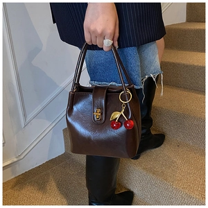 Détail d'un sac seau marron foncé avec fermoir métallique et breloque cerise rouge