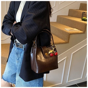Détail du sac seau en cuir marron foncé avec fermoir doré et accessoire cerise