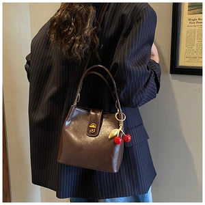 Détail du sac seau en cuir marron foncé avec fermoir doré et pendentif cerise
