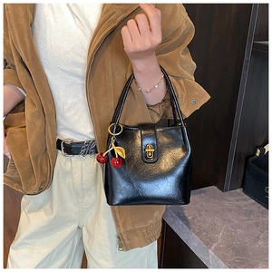 Détail d'un sac seau noir brillant avec fermoir doré et pendentif cerise élégant