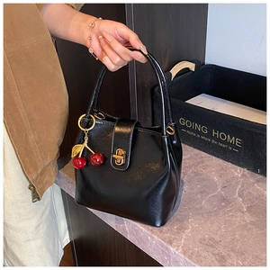 Détail d'un sac seau en cuir noir brillant avec un pendentif décoratif en cerise rouge
