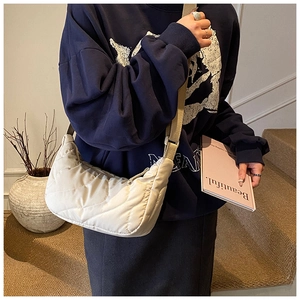 Detail of a beige quilted crescent shoulder bag with wide strap on a female model