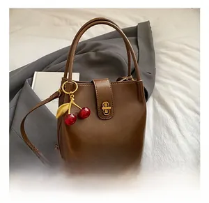 Détail du sac seau marron rétro montrant le cuir brillant et le charm cerise