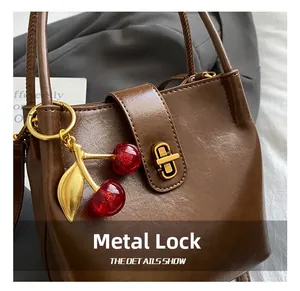 Détail du sac à main en cuir marron avec fermoir doré rotatif et breloque cerise