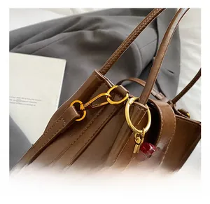 Détail d'un sac en cuir marron foncé avec crochets dorés et breloque cerise rubis
