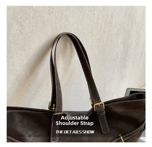 Detail of adjustable shoulder strap with brass buckle and white stitching on brown tote bag