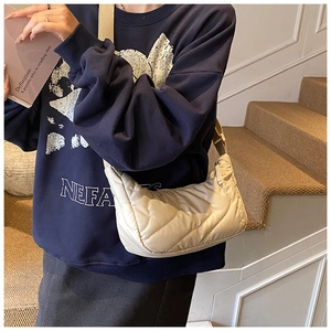 Detailed side view of beige quilted crescent bag worn by model in casual indoor setting