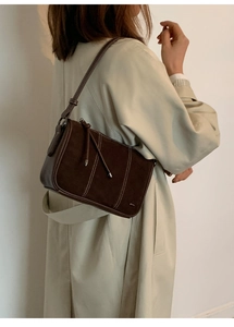Detail of dark brown suede shoulder bag with decorative white stitching and leather tassel