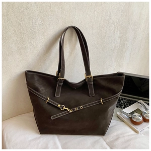 Detail of deep brown tote bag with matte texture and gold decorative buckles