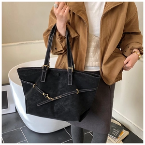 Detail of a large black suede tote bag with contrast stitching and gold metal hardware