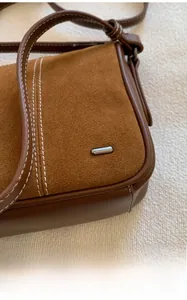 Detail of suede and leather stitching with silver hardware on a brown shoulder bag