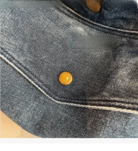 Detailansicht aus blauem Denim-Stoff mit polierter goldener Metallschnalle der Tasche