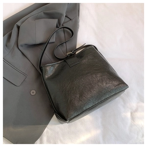 Detail of black textured leather tote bag on grey blazer and white fabric