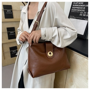 Detail of a brown oil-wax leather tote with a gold twist lock and adjustable strap
