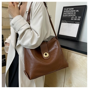 Detail of a brown leather tote bag with a gold ring clasp shown on a model