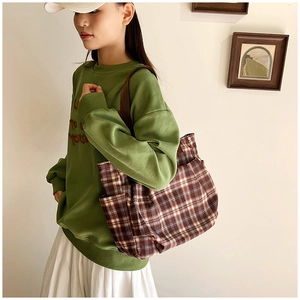 Detail of a large brown checkered canvas tote bag with a side pocket shown on a model