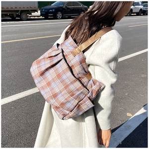 Detail view of plaid canvas tote bag with woven shoulder strap and pleated side texture