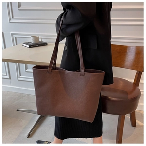 Close-up of brown leather tote bag showing fine lychee grain texture and minimalist straps