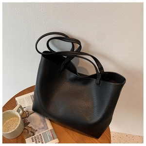 Close-up of black tote bag showing clear lychee grain leather texture and handle detail