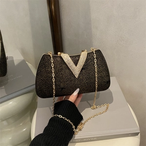 Elegant evening clutch bag with black fabric, golden radial patterns and V-shaped crystal buckle
