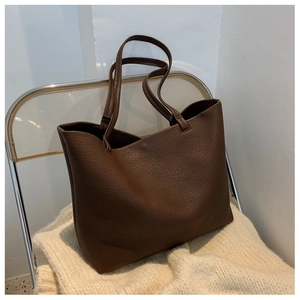 Detail of dark brown tote bag with lychee texture placed on a beige knitted sweater