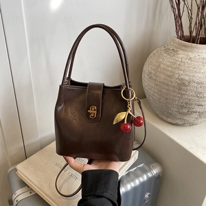 Sac seau rétro marron foncé avec fermoir doré et breloque cerise sur des livres