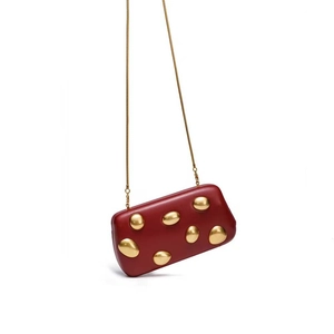 Close-up of red rectangular evening clutch with artistic golden stone accents and snake chain