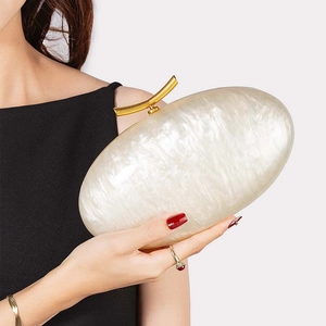 Detail of white marble acrylic shell clutch bag with gold branch clasp held by a model