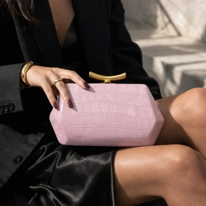 Pink crocodile pattern handbag with gold metal handle held by a model on stone stairs