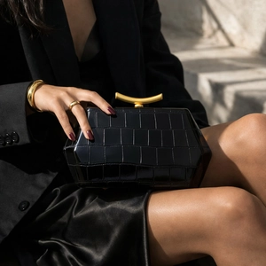Detail of black glossy crocodile pattern handbag with golden curved metal handle