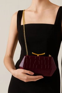 Detail of burgundy crocodile pattern clutch bag with gold chain and geometric metal clasp