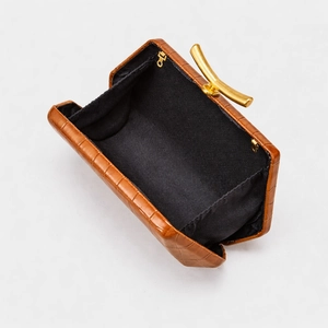 Macro detail of brown crocodile texture leather bag with elegant golden curved metal clasp