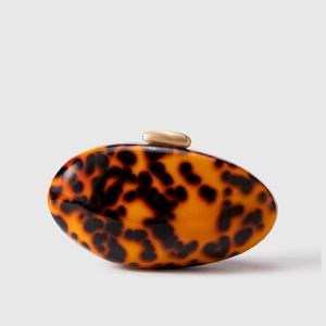 Macro detail of tortoiseshell acrylic clutch bag with golden pebble clasp