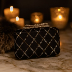 Macro detail of black evening clutch bag with gold rhinestone lattice and crystal bow